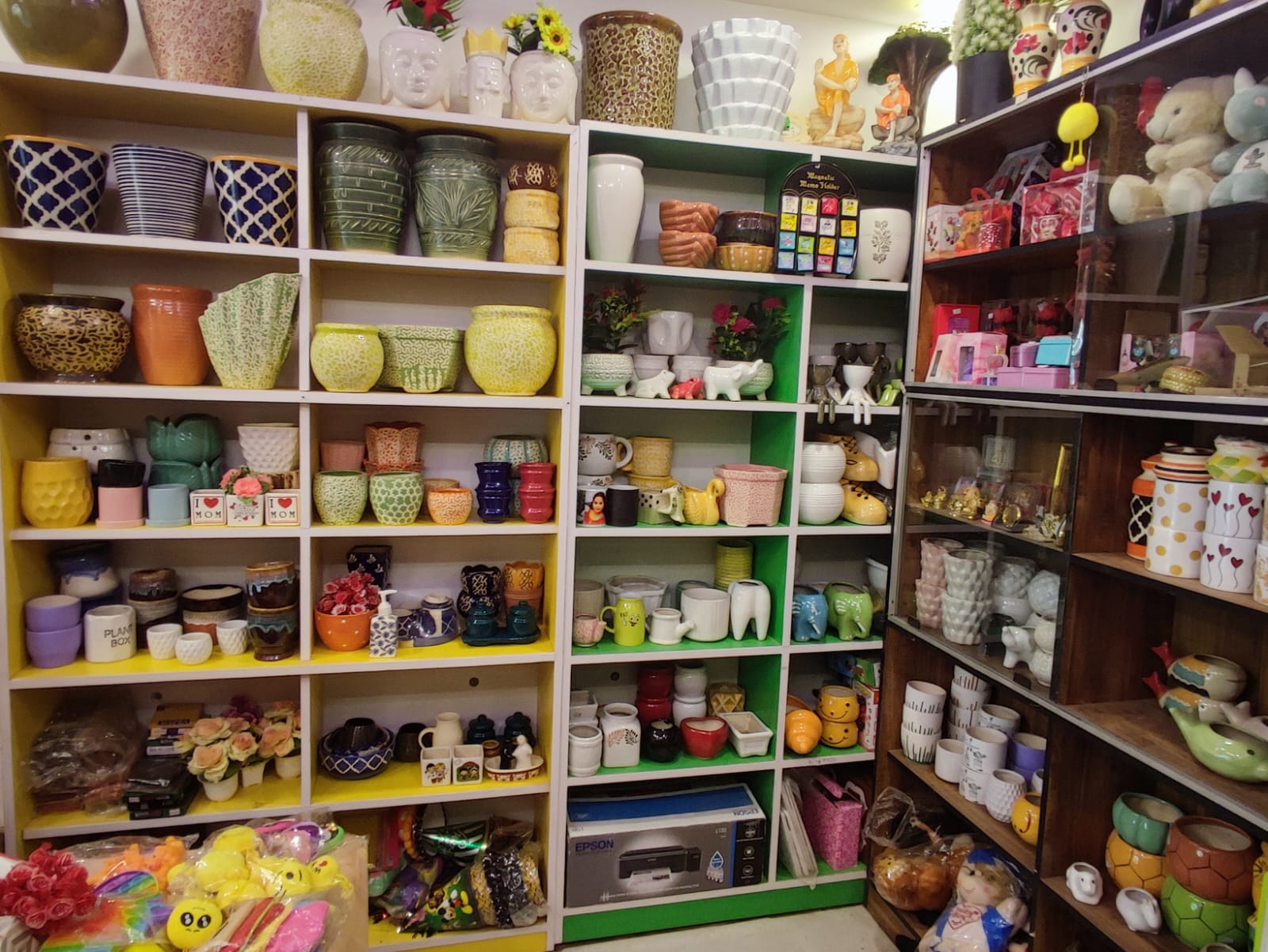 Display of assorted ceramic and resin planter pots at Silver Leaf Gift Shop in Trichy – colorful shelf arrangement featuring decorative flower pots, animal-shaped planters, and gifting items.